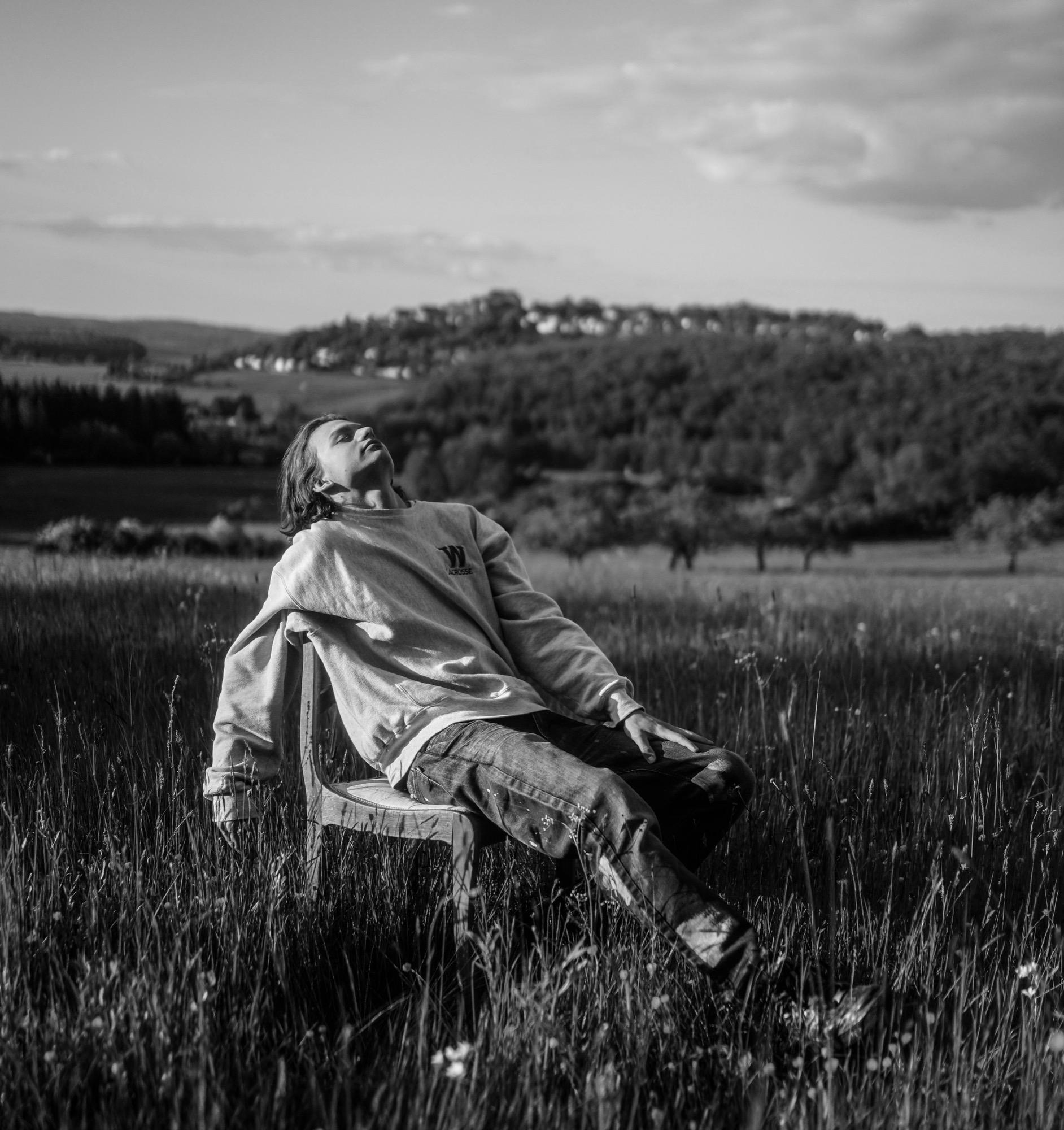 A man sitting back on a wooden chair in a meadow, face to the sky