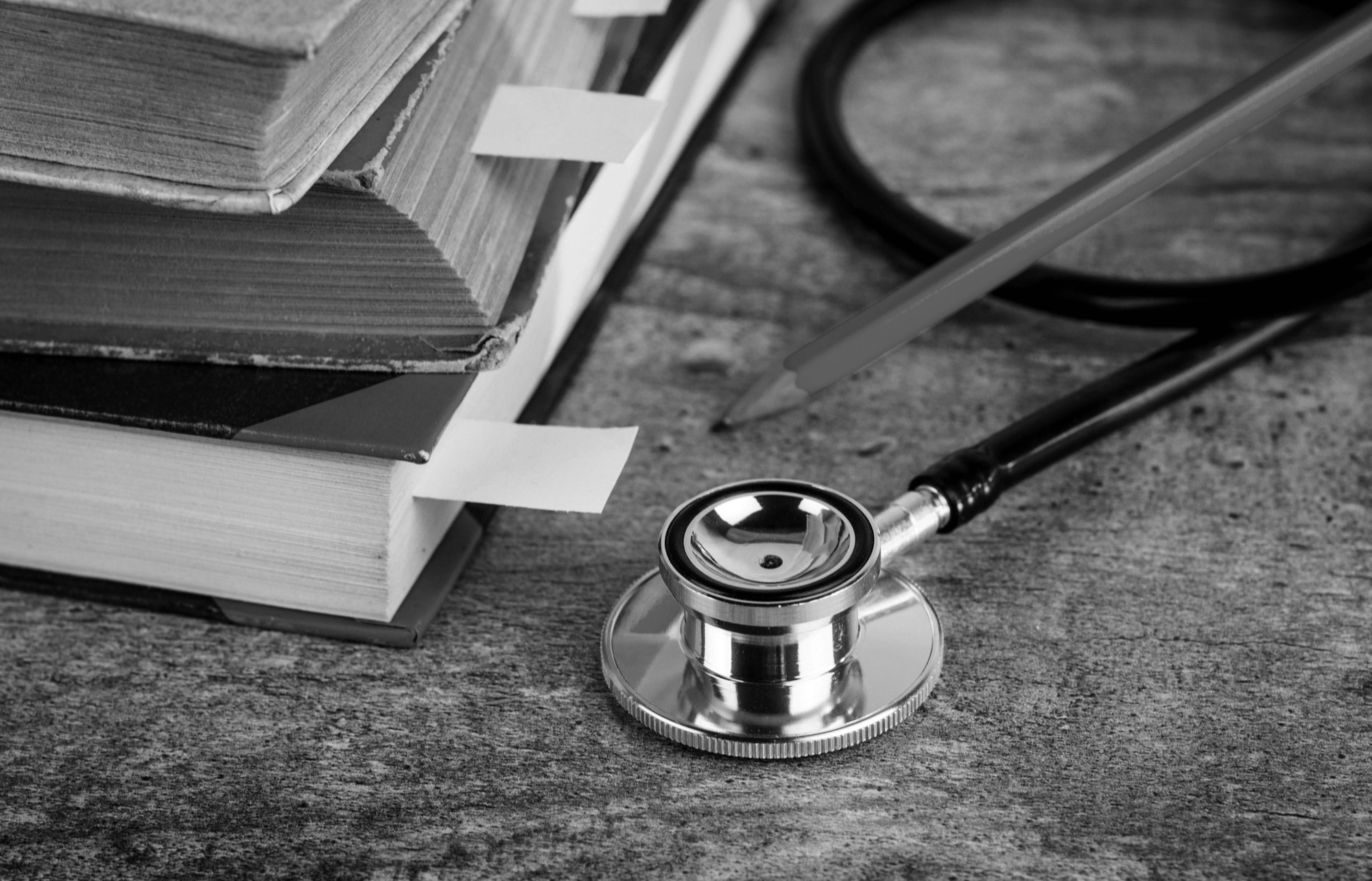 A stethoscope and a pencil beside a stack of old bookmarked books