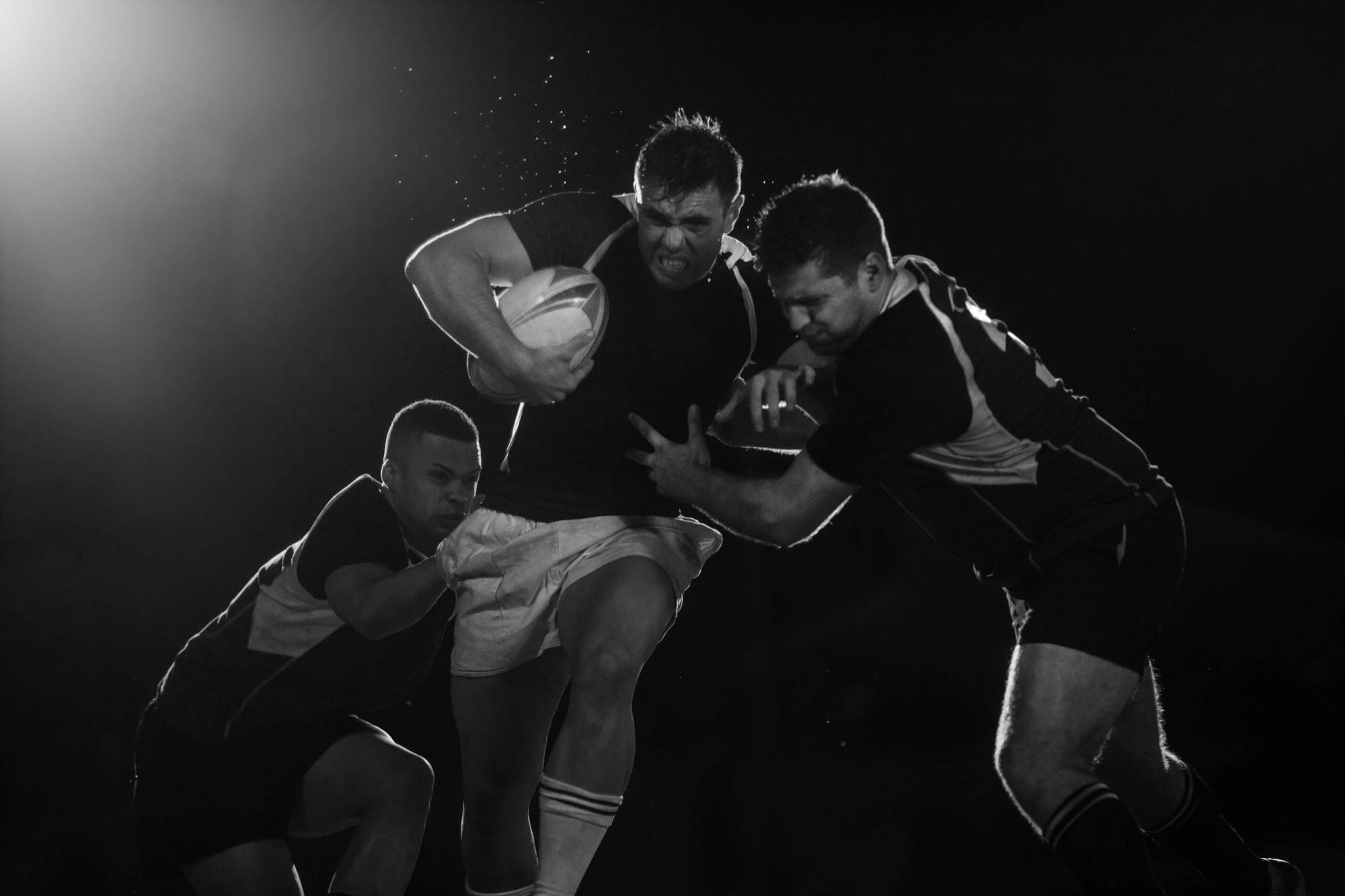 A rugby player charging forward with the ball as two defenders tackle him