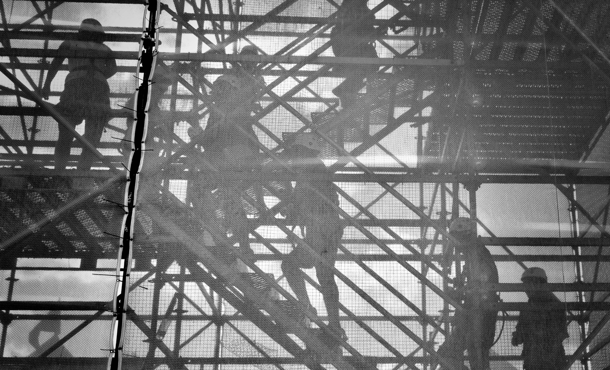 Workers on scaffolding seen through mesh, silhouetted against the light